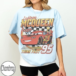 Peut inclure: T-shirt bleu clair avec un motif de Flash McQueen du film Cars. Le design comprend le texte "Lightning McQueen", "Cars", "Think Fast" et le num&eacute;ro "95". Le t-shirt a un aspect vintage et vieilli.