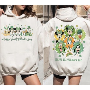 Puede incluir: Sudadera con capucha color crema con un diseño del Día de San Patricio. La parte delantera muestra personajes de dibujos animados con detalles verdes y el texto "Happy Saint Patrick's Day". La parte trasera muestra los mismos personajes dentro de tréboles, con el texto "Happy St. Patrick's Day."