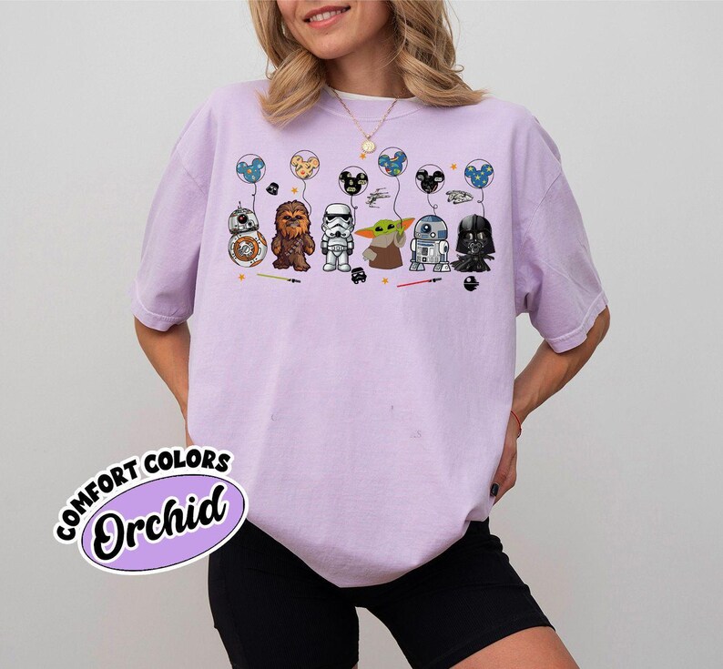 Peut inclure: T-shirt lilas avec des personnages de Star Wars en dessin anim&eacute; tenant des ballons. Les personnages incluent BB-8, Chewbacca, un Stormtrooper, Grogu, R2-D2 et Dark Vador. Le t-shirt porte les mots "COMFORT COLORS Orchid" en bas &agrave; gauche.