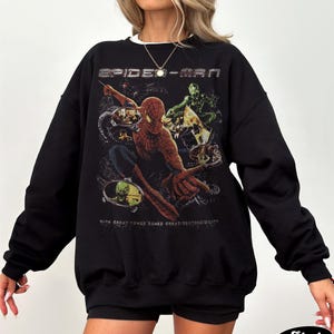 May include: Black Spider-Man sweatshirt featuring a graphic of Spider-Man and the Green Goblin. The text "SPIDER-MAN" is across the top, and "WITH GREAT POWER COMES GREAT RESPONSIBILITY" is below the graphic. The word "Black" is at the bottom.