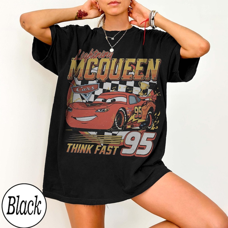 Peut inclure: T-shirt noir avec un motif de Flash McQueen du film Cars. Le design comprend le texte "Lightning McQueen", "Think Fast" et le num&eacute;ro "95". Le t-shirt a un aspect vintage et vieilli.
