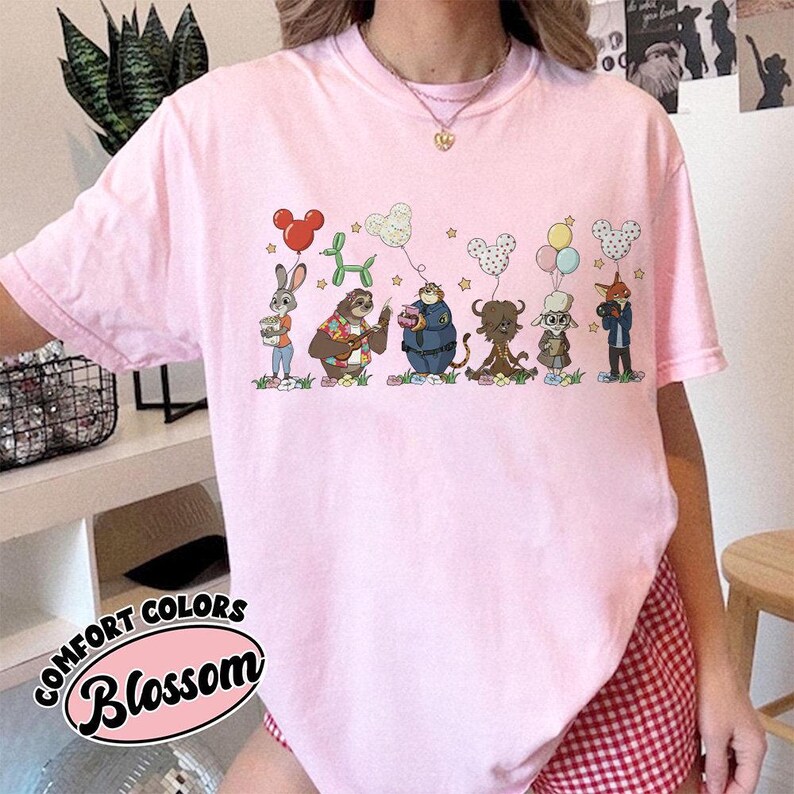 Puede incluir: Camiseta rosa Comfort Colors con un dise&ntilde;o de dibujos animados de personajes de animales con globos. El texto "Blossom" est&aacute; impreso en cursiva. La camiseta tiene cuello redondo y mangas cortas.
