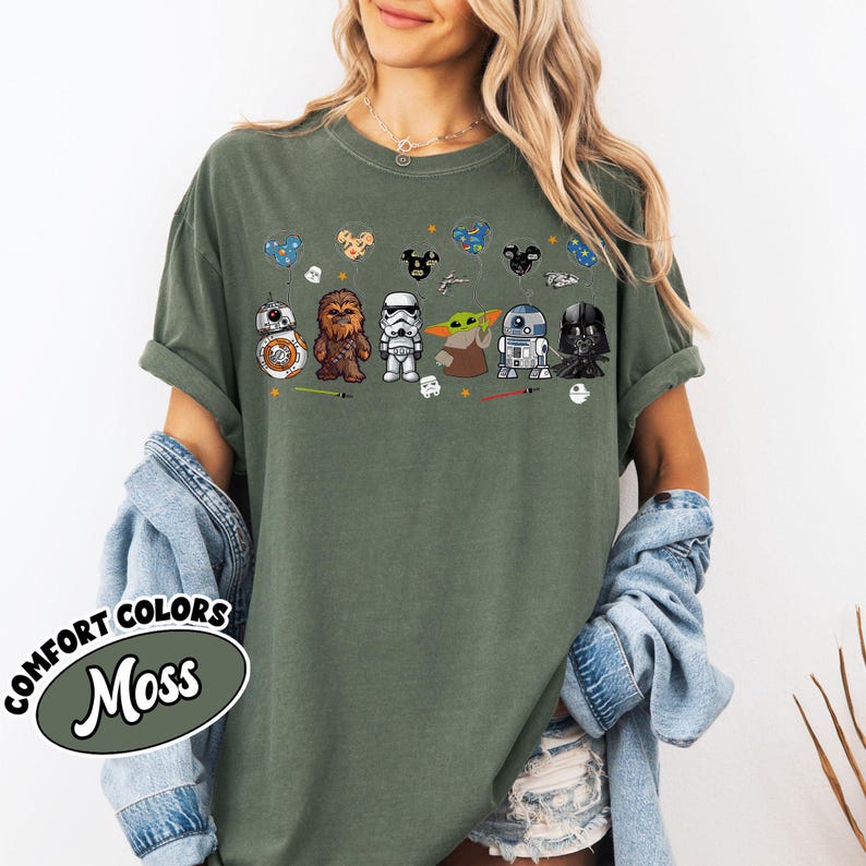 Peut inclure: T-shirt vert mousse avec des personnages de dessins anim&eacute;s de Star Wars. Le motif comprend BB-8, Chewbacca, un Stormtrooper, Grogu, R2-D2 et Dark Vador. Le t-shirt a des manches retrouss&eacute;es et les mots "COMFORT COLORS" et "Moss" dans un ovale.