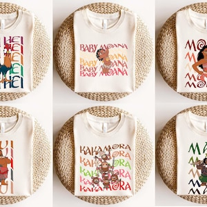 May include: Six off-white t-shirts with colorful graphics and text from the movie Moana. The designs include characters like Hei Hei, Baby Moana, Moana, Maui, and the Kakamora. Each shirt is displayed on a round, woven surface.