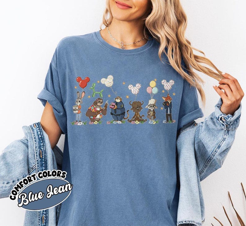 Puede incluir: Camiseta azul Comfort Colors con una fila de personajes de animales de dibujos animados y globos. Los personajes incluyen un conejo, un perezoso, un oso, un toro, un b&uacute;ho y un zorro. La camiseta tiene las palabras "Comfort Colors Blue Jean".