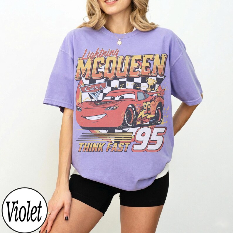 Peut inclure: T-shirt violet avec un motif de Flash McQueen du film Cars. Le design comprend le texte "Lightning McQueen", "Cars", "95" et "Think Fast". Le t-shirt a des manches courtes et une coupe ample.