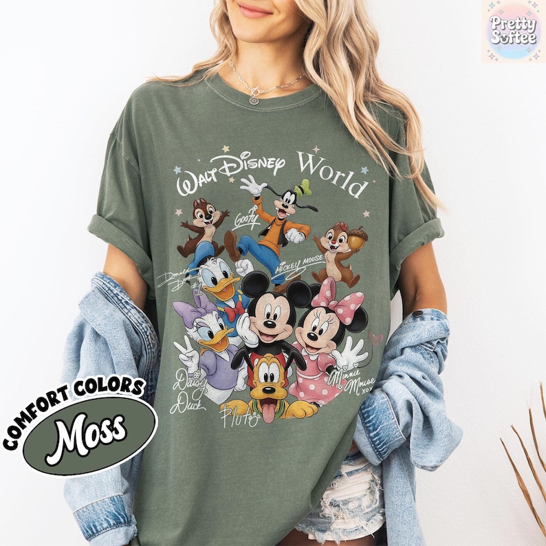 May include: Moss green t-shirt featuring a graphic of Disney characters, including Mickey and Minnie Mouse, Donald Duck, and Goofy. The text "Walt Disney World" is printed above the characters. The shirt also has the text "COMFORT COLORS" and "Moss".