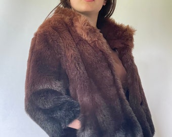 May include: A brown and black ombre faux fur jacket with a collar. The jacket has a zipper closure and pockets.