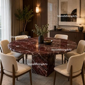 Può includere: Un tavolo da pranzo rotondo con piano in marmo rosso intenso e base quadrata abbinata. Sei sedie imbottite beige con struttura in legno circondano il tavolo. La stanza ha un design moderno con una palette di colori neutri.