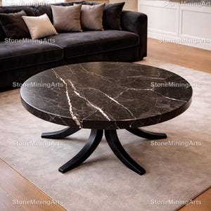 May include: A round coffee table with a black marble top featuring white veining. The table has a black, pedestal-style base. The table is set on a light gray rug in a living room setting.