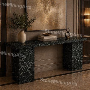 Puede incluir: Una consola de mármol negro con vetas blancas. La mesa tiene una tapa rectangular y dos patas cuadradas. Un jarrón beige con vegetación, libros y objetos decorativos se encuentra sobre la mesa. La mesa está en una habitación con paneles de madera oscura.