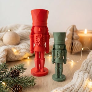 May include: Two decorative nutcracker figurines, one red and one green, stand on a wooden surface. The red nutcracker is larger, while the green one is smaller. Both have detailed uniforms and hats, ideal for festive decorations.