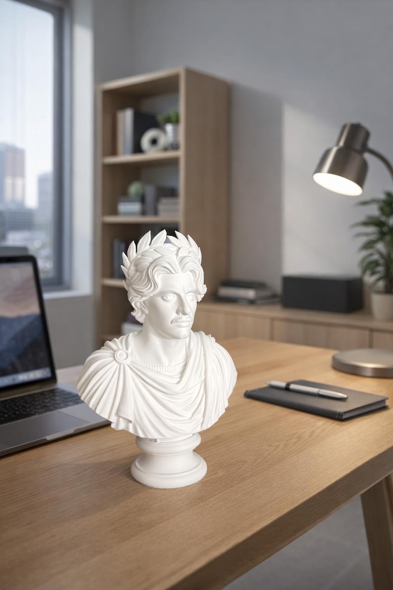 May include: A white bust sculpture of a person with wavy hair wearing a laurel wreath and a draped toga. The figure has a calm facial expression and is mounted on a circular pedestal base, showcasing detailed folds in the fabric and hair texture.