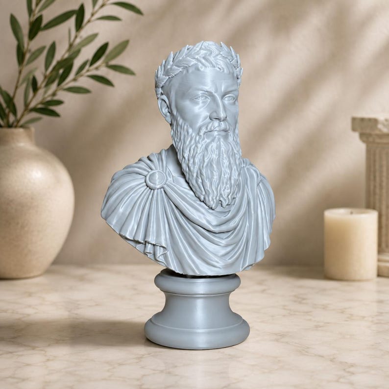 May include: A light gray bust sculpture of a bearded man wearing a laurel wreath on his head and a draped toga fastened with a circular brooch at the shoulder. The figure is mounted on a smooth, circular pedestal base with a matte finish.