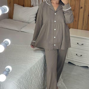 Peut inclure: Un ensemble de pyjama deux pi&egrave;ces marron clair. Le haut est boutonn&eacute; avec une bordure blanche sur le col et les poignets. Le pantalon assorti est &agrave; jambes larges. L'ensemble est fait d'une mati&egrave;re douce et confortable.