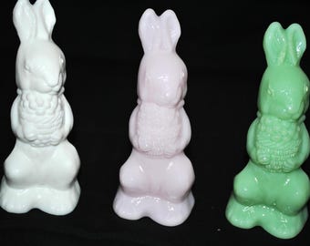 Pode incluir: Três estatuetas de coelho de vidro, cada uma segurando um buquê de flores. Os coelhos são brancos, rosa e verdes.