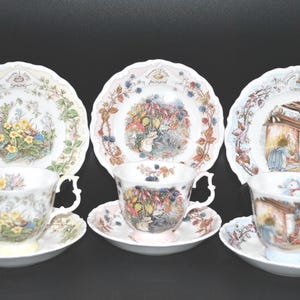 May include: Three white porcelain tea sets, each featuring a saucer and cup with scalloped edges. The sets are decorated with colorful illustrations of animals and seasonal themes labeled Spring, Autumn, and Winter, including floral and berry motifs.