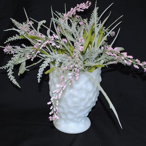 Puede incluir: Un jarrón de vidrio de leche blanco con una superficie texturizada, lleno de un ramo de flores artificiales rosas y verdes.