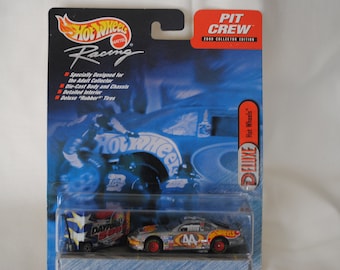 May include: A silver Hot Wheels Deluxe diecast car with a black and red racing design and the number 44 on the side. The car is on a blue and white background with the words "Hot Wheels Deluxe" and "Pit Crew" on the packaging.