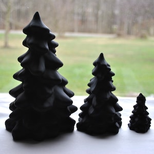 May include: Three black ceramic Christmas trees of varying sizes. The largest tree is about 10 inches tall, the middle tree is about 6 inches tall, and the smallest tree is about 4 inches tall.