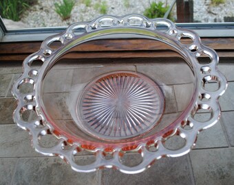 Pode incluir: Uma tigela de servir de vidro transparente com um tom rosado e uma borda festonada. A tigela tem um padrão decorativo de raios de sol no fundo.