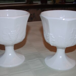 Puede incluir: Dos copas de vidrio de leche blanco con un diseño de vid. Las copas tienen una base con pie y están hechas de vidrio blanco opaco.