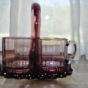 May include: A set of two amethyst glass creamer and sugar containers with a handle, featuring a ribbed design and a scalloped base.