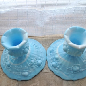 Puede incluir: Dos candelabros de vidrio azul claro con un borde con volantes y un diseño floral. Los candelabros tienen una base redonda y una parte superior acampanada. El vidrio tiene un patrón de remolino blanco. Los candelabros son vintage y decorativos.