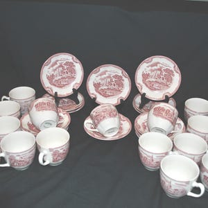 May include: A set of 14 vintage teacups and saucers with a pink floral pattern. The cups and saucers are white with a pink floral design. The set includes 7 teacups and 7 saucers.