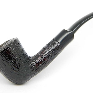 Peut inclure: Une pipe en bruyère noire avec une finition texturée. La pipe a une tige incurvée et une coupe légèrement plus large que la tige.