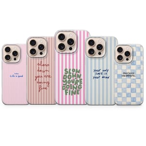 Pode incluir: Cinco capas de telemóvel em tons pastel de rosa, azul e branco. Cada capa tem um design único com textos como "Life is good" e "Slow down you are doing fine". As capas têm vários padrões.
