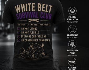 May include: A black short-sleeve t-shirt featuring the text "WHITE BELT SURVIVAL CLUB" in beige and purple. Below, a checklist reads: "THINGS I LEARNED THIS WEEK", "I'M NOT STRONG", "I'M NOT FLEXIBLE", "EVERYONE CAN CHOKE ME", "I'M COMING BACK TOMORROW".