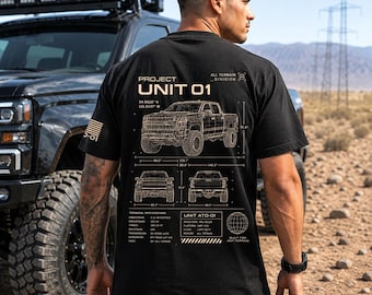 May include: Black t-shirt with a detailed schematic of a truck, labeled "Project Unit 01" and "All Terrain Division." The design includes technical specifications and a globe graphic. The shirt is worn by a person standing near a black truck.