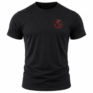 Puede incluir: Una camiseta negra de manga corta con un peque&ntilde;o gr&aacute;fico en la parte superior izquierda del pecho. El gr&aacute;fico consiste en un contorno rojo de cara sonriente parcialmente dividido, revelando un dise&ntilde;o de calavera oscuro y detallado.