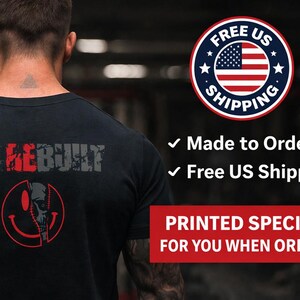 Puede incluir: Una camiseta negra con el texto I'M REBUILT en letras grises y rojas desgastadas en la parte posterior. Debajo del texto hay un gr&aacute;fico rojo de una cara sonriente dividida con un dise&ntilde;o de calavera. La camiseta se muestra desde atr&aacute;s.
