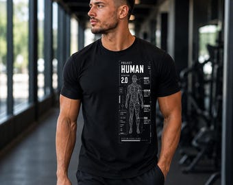 May include: A black short-sleeved t-shirt featuring a white graphic print on the chest. The design includes the text "PROJECT HUMAN VERSION 2.0" above a wireframe anatomical human figure, surrounded by technical labels and data points.