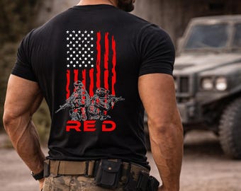 May include: A black short-sleeved t-shirt featuring a graphic on the back. The design displays a stylized American flag with red vertical stripes and white stars, accompanied by two soldiers in tactical gear and the word RED in bold red letters.