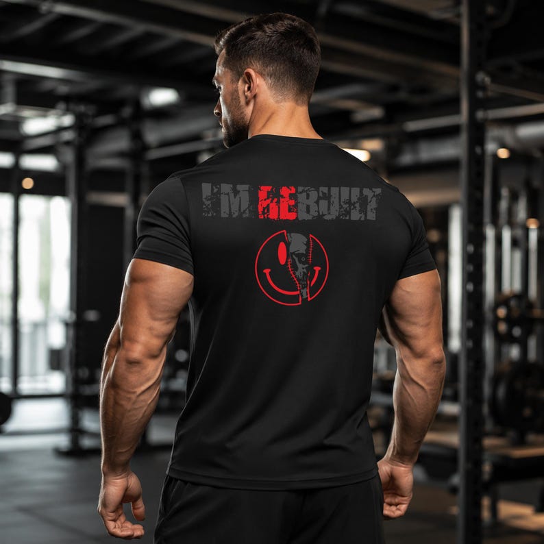 Puede incluir: Una camiseta negra de manga corta con el texto I'M REBUILT en letras grises y rojas en la parte superior de la espalda. Debajo del texto hay un gr&aacute;fico rojo de una cara sonriente con un dise&ntilde;o de calavera a la derecha, dividido por una l&iacute;nea.
