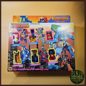 May include: A Construction Bot toy set in original packaging featuring six individual robot figures labelled Mixer-Bot, Digger-Bot, Bulldozer-Bot, Fork Lift-Bot, Shovel-Bot, and Tow Truck-Bot. The box displays colourful illustrations of robots against a desert and city skyline background.