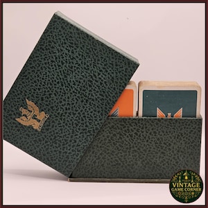 Könnte beinhalten: Vintage dunkelgrüne Kartenspielbox mit strukturierter Oberfläche und goldenem Emblem. Die Box ist geöffnet und zeigt einen Stapel Karten mit orangefarbenen und tealfarbenen Designs. Die Box ist mit "SERVICE" beschriftet.