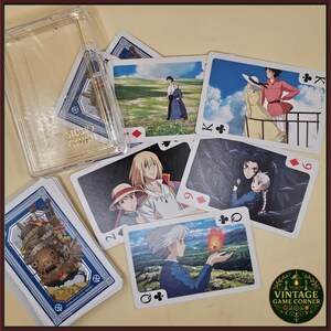 May include: A deck of playing cards featuring images from the animated film "Howl's Moving Castle." The cards are displayed with a clear plastic case and a "Studio Ghibli" logo. The deck has a blue border and the "Vintage Game Corner" logo.