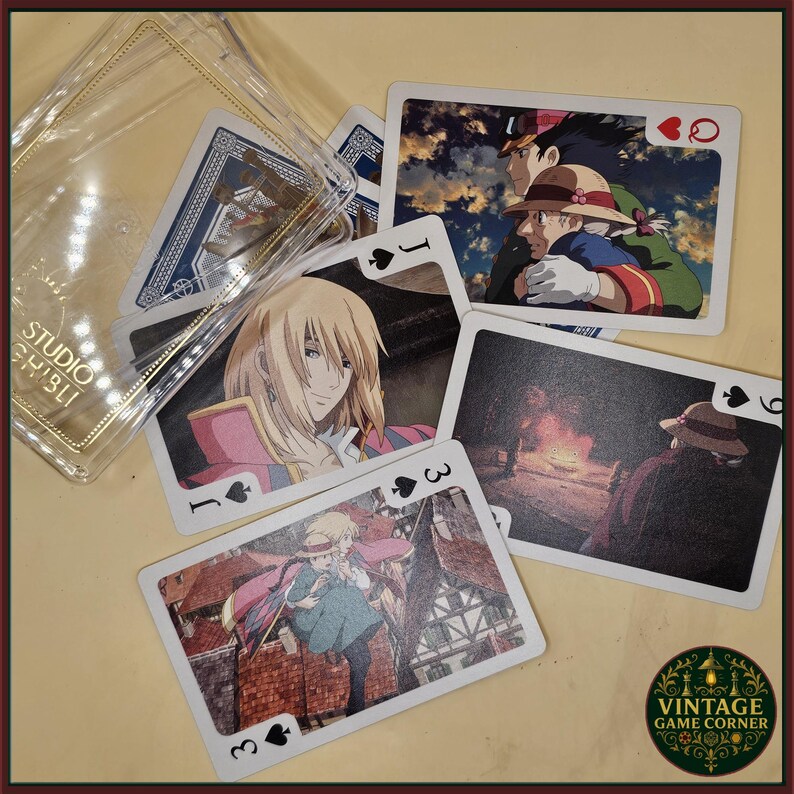 May include: Playing cards featuring characters from the Studio Ghibli film, "Howl's Moving Castle." The cards display various scenes and characters, including Howl and Sophie. The cards are in a clear plastic case with "Studio Ghibli" printed on it.