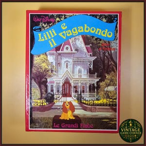 May include: A vintage Disney "Lady and the Tramp" Italian edition book cover. The cover features a large white house with a red roof, a cartoon dog, and the title "Lilli e il Vagabondo" in blue. The book is framed in red.