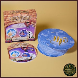 May include: A Harry Potter themed card game set featuring a square box with brick-patterned graphics, a round game rules card, and a stack of round blue playing cards. The box displays the text Harry Potter, With Special Glitter Card, and Round Playing Cards.