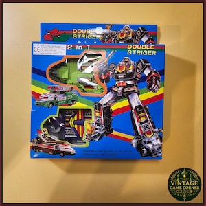 May include: A 2 in 1 Double Striger toy box featuring a large black, silver, and red robot illustration. The blue packaging displays a green vehicle, a red and white vehicle, and a black and red vehicle. Text includes 2 in 1 and Double Striger.