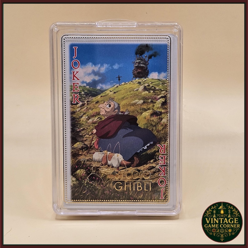 May include: A Studio Ghibli Joker playing card featuring an illustration of a character from the movie Howl's Moving Castle. The card is in a protective case. The word "Joker" is printed vertically on the left and right sides of the card.