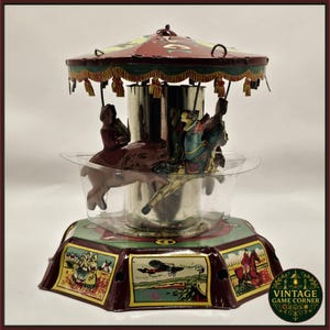 May include: A vintage carousel toy with a red and green canopy, featuring figures riding animals. The base has colourful panels with illustrations. The toy is made of metal and has a clear plastic bowl. A classic toy.
