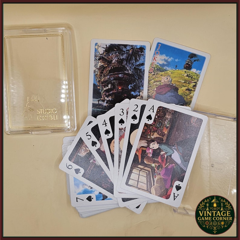 May include: A deck of playing cards featuring illustrations from a movie, with a clear plastic case. The cards are fanned out, displaying various suits and face cards. The Joker cards show a large, detailed image. The case has the text "STUDIO GHIBLI".