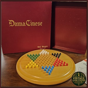 Puede incluir: Juego de mesa Dama Cinese vintage. El tablero de juego de madera es redondo con agujeros para las clavijas. Las clavijas son de varios colores. La caja roja tiene letras doradas que dicen "Dama Cinese".