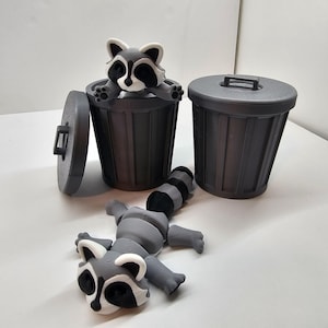May include: Gray trash cans with a raccoon figurine. One raccoon is peeking out of a trash can, another is lying on the surface, and the third trash can has a lid. The raccoon has a black mask and a striped tail.